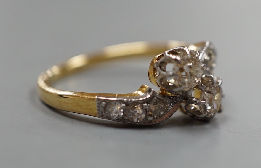 A yellow metal and two stone diamond set crossover ring, with diamond set shoulders, size J, gross weight 3.1 grams.